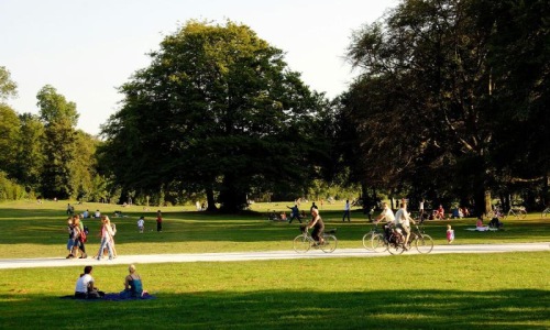 A park with many people riding bikes, having a picnic, and walking.